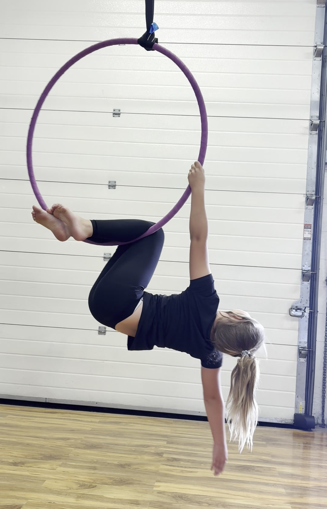 Junior aerial student practising an inverted shape on a purple hoop